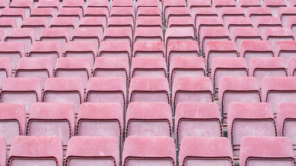 Empty and weathered worn down stadium seating in lightened red and pink tones after year of exposure to weather outdoors in daylight. background graphic design resource