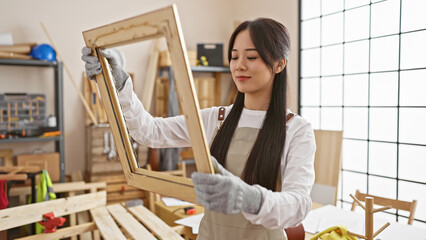 A young asian woman examining a wooden frame in a bright carpentry workshop