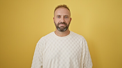 Handsome young man, with a concentrated expression, nonchalantly standing against an isolated yellow background, exudes coolness while looking right into the camera.