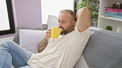 Handsome young man in deep thought, sitting comfortably at home, sipping coffee on a relaxing morning.