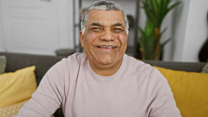 A smiling middle-aged man with grey hair, casually dressed, sits in a cozy, stylish living room.