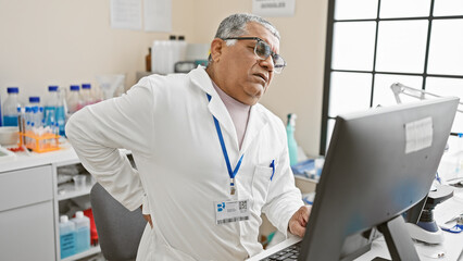 Mature man with grey hair in lab coat experiencing back pain at work in a laboratory setting