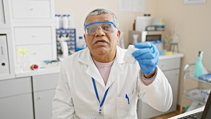 Mature grey-haired man in lab coat and gloves analyzing a sample in a laboratory setting, portraying healthcare and scientific research themes.