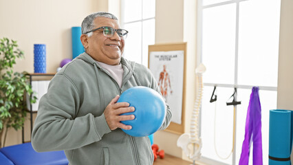 Smiling senior man exercising with a blue ball in a rehabilitation clinic