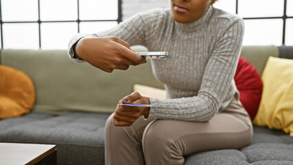 Young adult african american woman with curly hair photographing credit card indoors