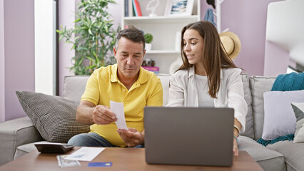 Father and daughter sitting together on sofa, confidently accounting their family finances with a...