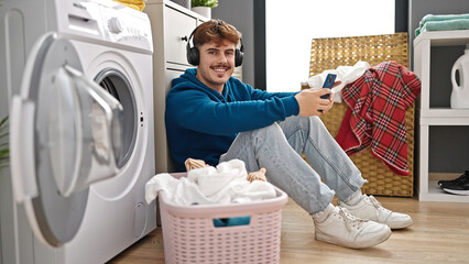 Young hispanic man listening to music washing clothes at laundry room