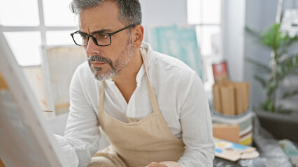 Handsome young hispanic grey-haired man artist, fully engrossed, drawing seriously in art studio - obrazy, fototapety, plakaty