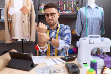 Hispanic man with beard dressmaker designer working at atelier suffering pain on hands and fingers,...
