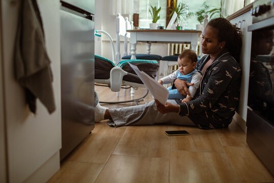 Single young mother holding her baby son going over bills and home finances in the kitchen at home