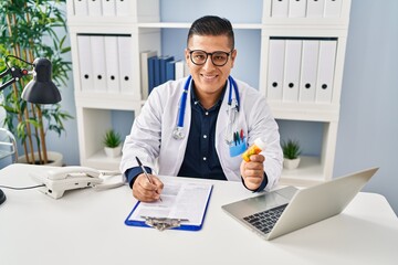 Young latin man doctor writing on document holding pills at clinic