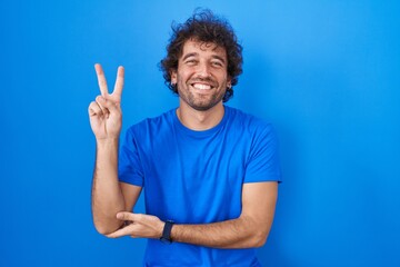 Hispanic young man standing over blue background smiling with happy face winking at the camera...