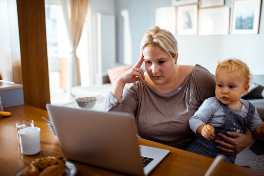 Young worried single mother using a laptop with her baby toddler son in her lap