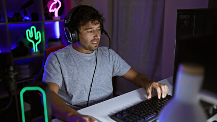 Focused man gaming in a dark room with neon lights, headphones on, intensely looking at the computer screen.