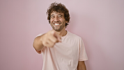 Handsome young hispanic man laughing and pointing in a friendly manner against a pink isolated...