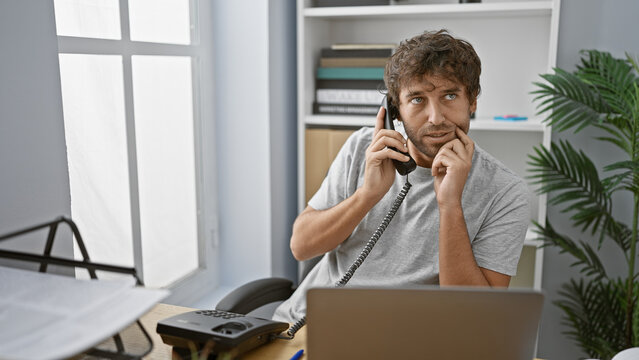 A handsome hispanic man with a beard and green eyes makes a phone call in a modern office interior.
