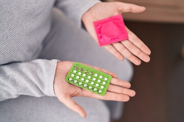 Young beautiful plus size woman holding birth control pills and condom at home