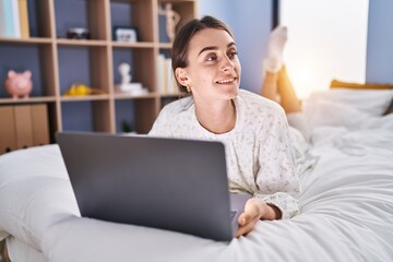 Young caucasian woman using laptop lying on bed at bedroom