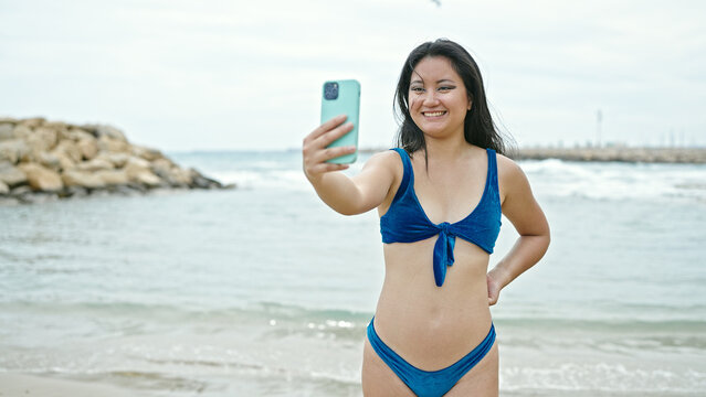 Young chinese woman tourist wearing bikini make selfie by smartphone at the beach