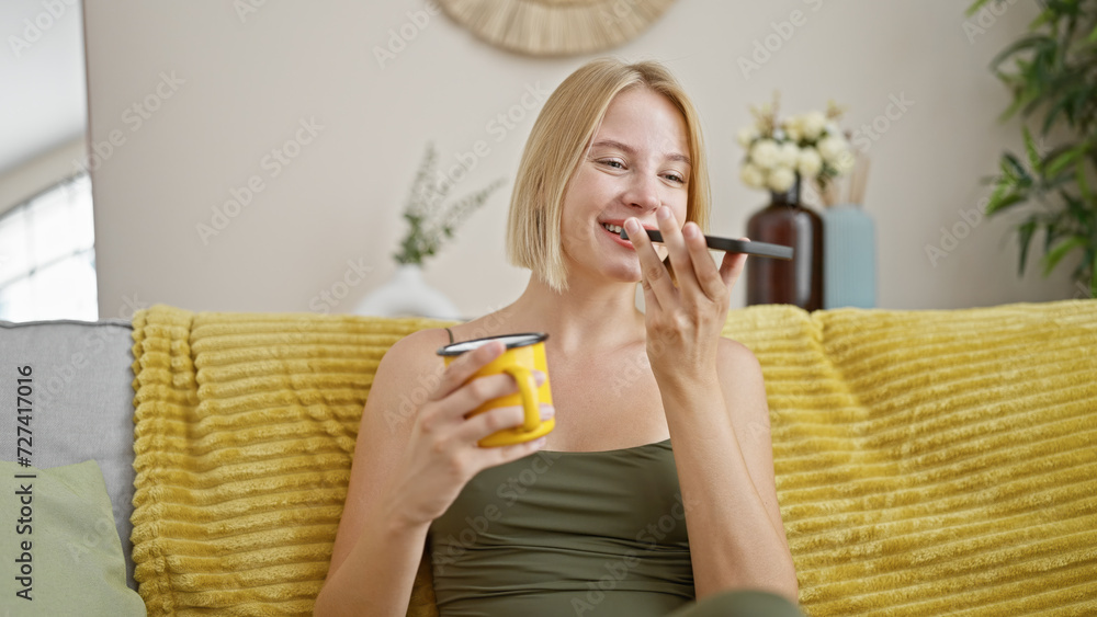 Canvas Prints Young blonde woman sending voice message with smartphone drinking coffee at home