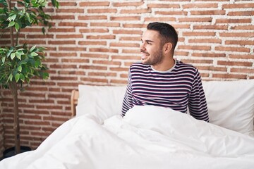 Young hispanic man smiling confident sitting on bed at bedroom