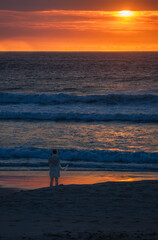 A female standing at the beach and enjoing the a golden sunset at the sunset beach, Cape Town, South Africa