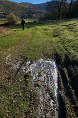 a mountaineer walks along a path with frozen puddles