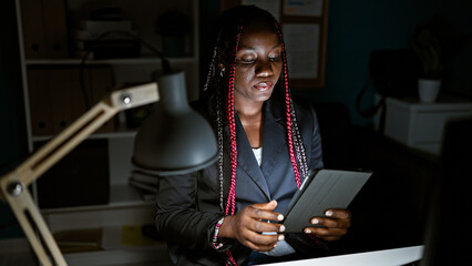 Focused african american woman worker at office, monitors aglow, braids and dark jacket on, nimble...