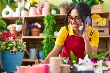 Young beautiful arab woman florist talking on smartphone writing on notebook at flower shop