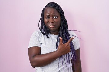 Young african woman standing over pink background pointing aside worried and nervous with...