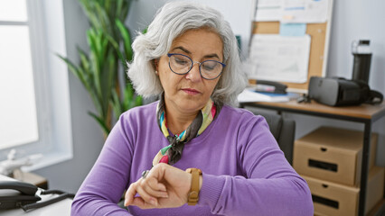 Mature woman checking time in modern office setting, conveying punctuality and professionalism.