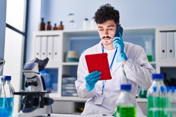 Fototapeta na wymiar Young caucasian man scientist using touchpad talking on smartphone at laboratory