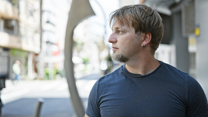 Handsome caucasian adult man with a beard and blond hair contemplating in an urban city street setting.