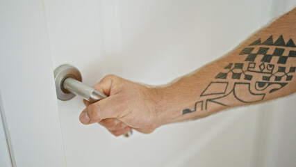 Close-up of a tattooed man's hand turning a door knob inside a bright home environment.