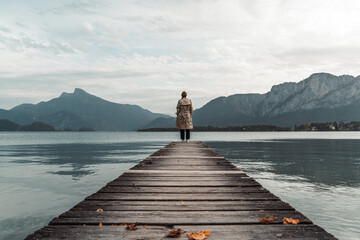 a lady standing on a pier of a mountain lake