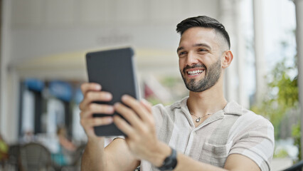 Young hispanic man smiling confident using touchpad at coffee shop terrace