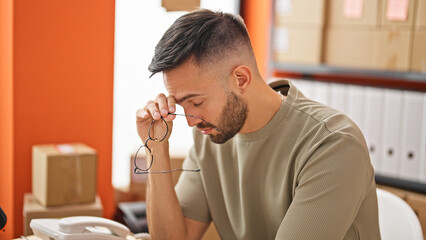 Young hispanic man ecommerce business holding glasses stressed at office