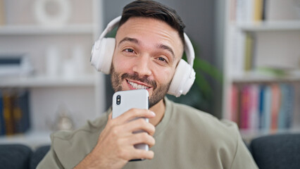 Young hispanic man listening to music singing song at home