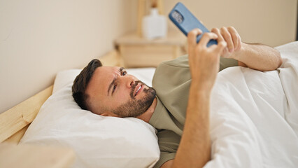 Obraz na płótnie Canvas Young hispanic man using smartphone lying on bed at bedroom