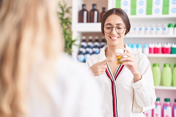 Young beautiful hispanic woman customer holding pills speaking with pharmacist at pharmacy