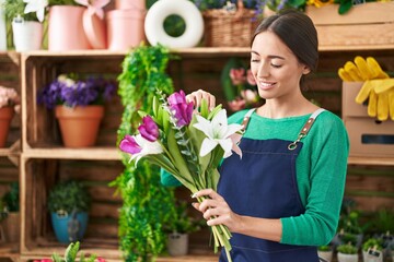 Young beautiful hispanic woman florist holding bouquet of flowers at flower shop