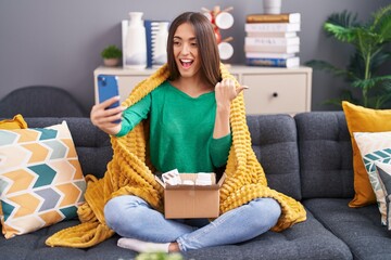 Young sick hispanic woman doing video call with doctor pointing thumb up to the side smiling happy with open mouth