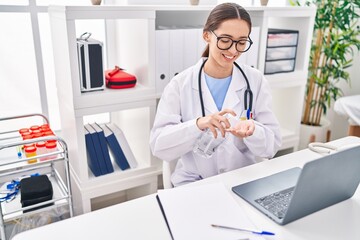 Young beautiful hispanic woman doctor using sanitizer gel hands at clinic