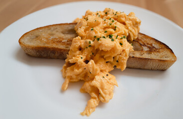Scrambled egg served across a slice of buttered sourdough toast on a white plate. - 727421634