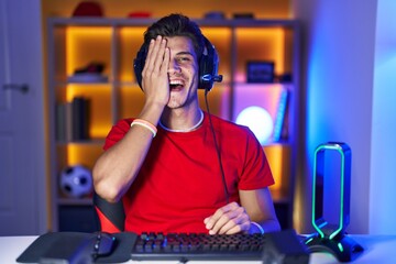 Young hispanic man playing video games covering one eye with hand, confident smile on face and surprise emotion.