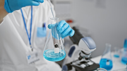 Caucasian male scientist pipetting blue liquid into a flask in a laboratory setting