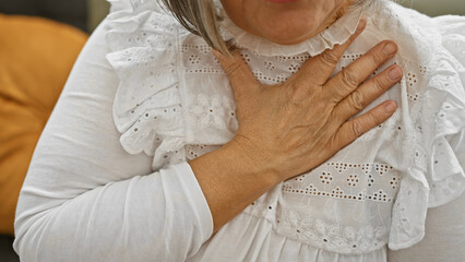 Mature woman experiencing chest pain while sitting in a living room.