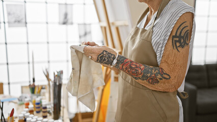 Indoor art school's joy, hands of senior woman artist lovingly cleaning paintbrushes amidst...