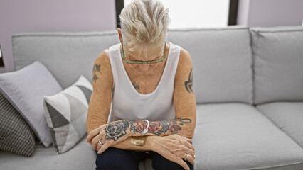 Perturbed mature grey-haired woman chilling solo on her cozy sofa at home, engrossed in deep thought