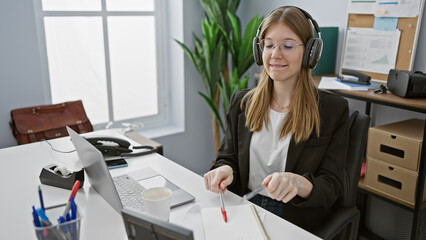 Obraz na płótnie Canvas A professional young woman wearing glasses and headphones focused on her work in a modern office setting